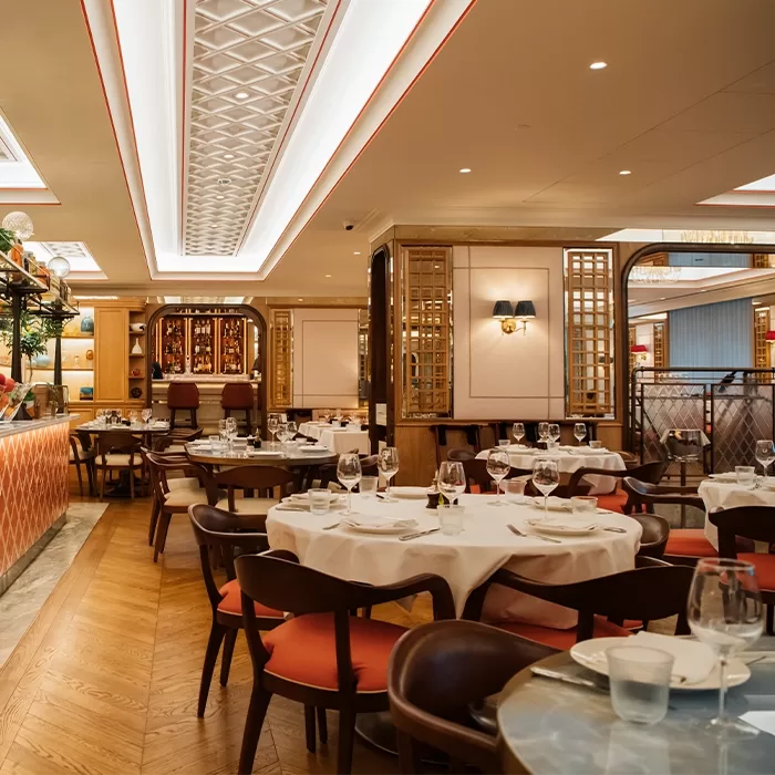 A stylish, modern restaurant interior with round tables set for dining, wooden chairs with orange cushions, elegant lighting, and decorative wooden partitions creating a warm, inviting atmosphere.