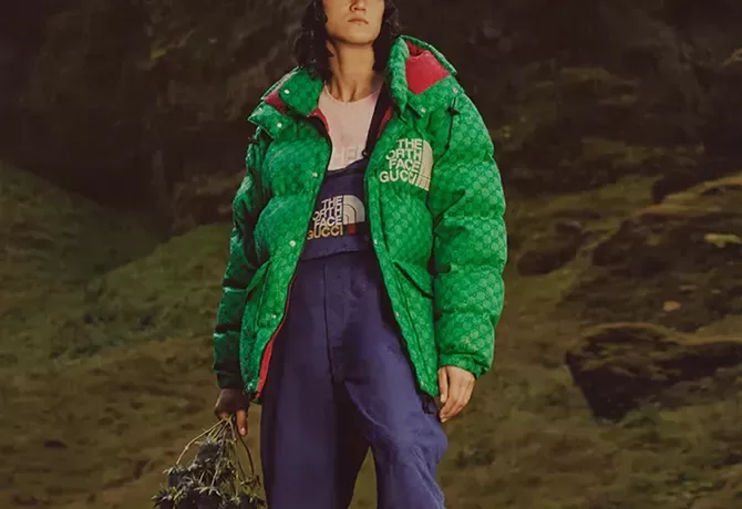 Male model in North Face x Gucci fashion clothing stood in front of green landscape