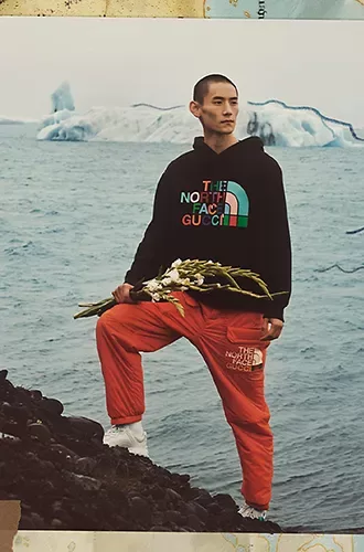 Male model in North Face x Gucci fashion clothing stood on rocks in front of icy sea background